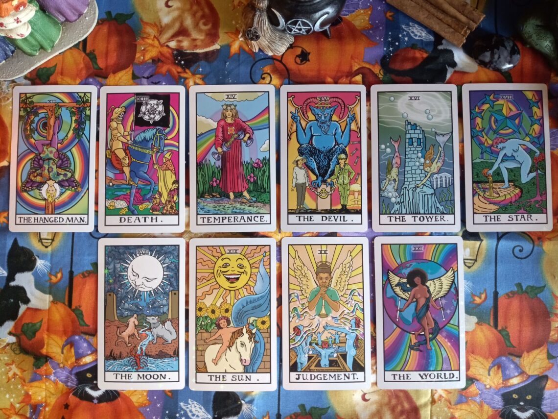 A vibrant arrangement of tarot cards laid out in two neat rows on an autumn-themed tablecloth. The tarot cards include The Hanged Man, Death, Temperance, The Devil, The Tower, The Star, The Moon, The Sun, Judgement, and The World—each illustrated with rich, symbolic artwork.