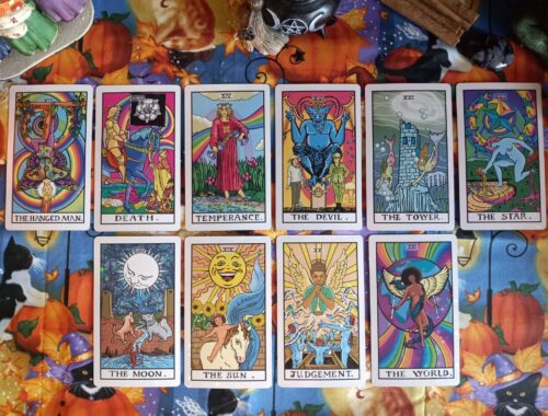A vibrant arrangement of tarot cards laid out in two neat rows on an autumn-themed tablecloth. The tarot cards include The Hanged Man, Death, Temperance, The Devil, The Tower, The Star, The Moon, The Sun, Judgement, and The World—each illustrated with rich, symbolic artwork.